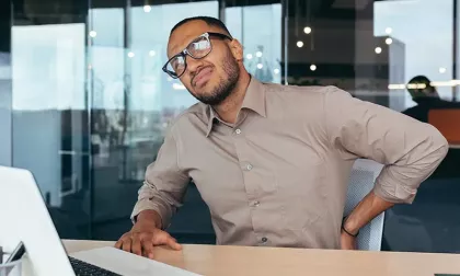 man sitting at desk holding back in pain