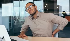 man sitting at desk holding back in pain